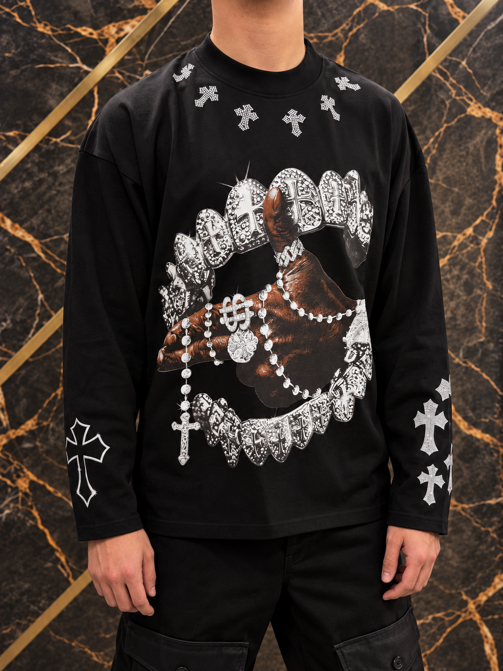 Maglia nera a maniche lunghe con croci indossata, inquadratura senza volto su sfondo nero e oro — immagine rielaborata
