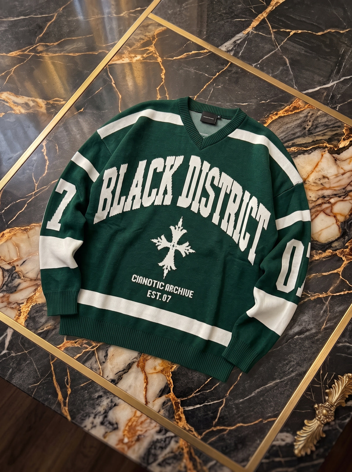 Maglione verde con scollo a V, scritta Black District e dettagli avorio, fotografia reale del capo
